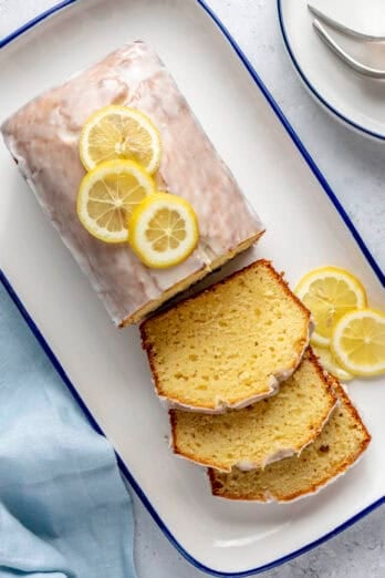 Lemon bread topped with glaze after firming up with a few slices cut and laying flat, loaf topped with fresh thin lemon slices.