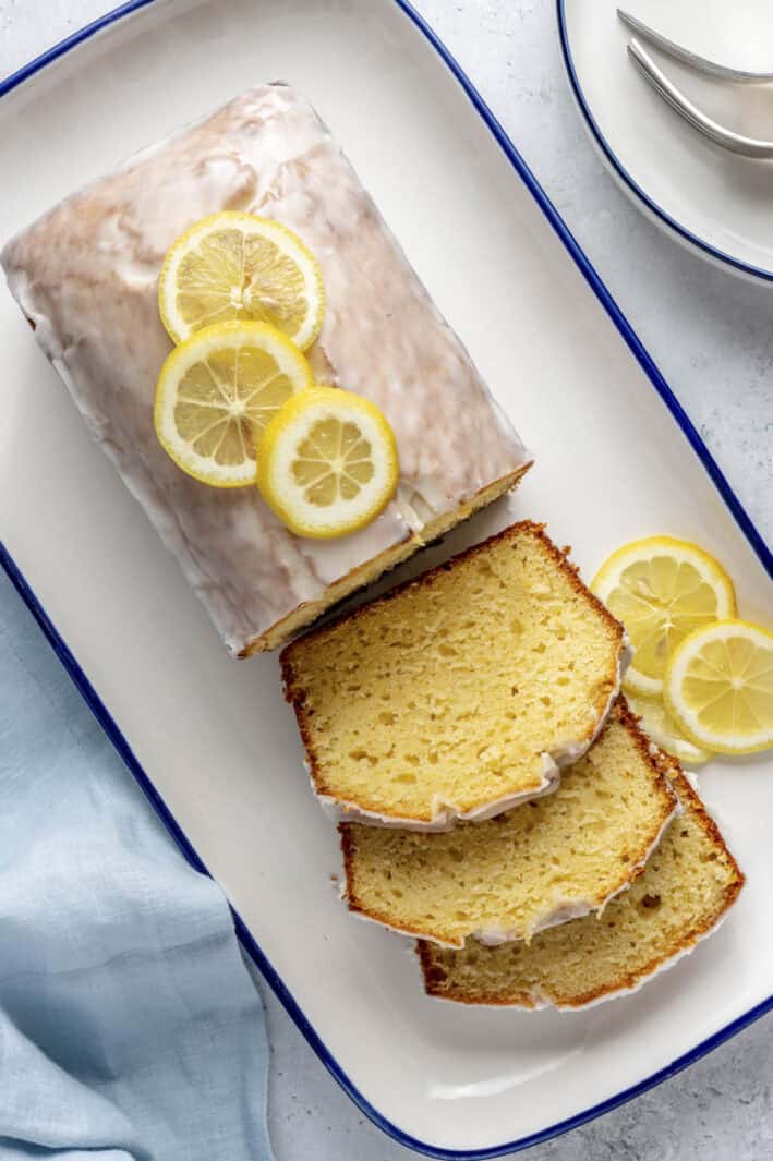 Lemon bread topped with glaze after firming up with a few slices cut and laying flat, loaf topped with fresh thin lemon slices.