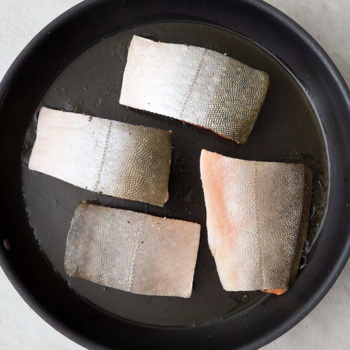 Seasoned salmon in an oiled skillet.