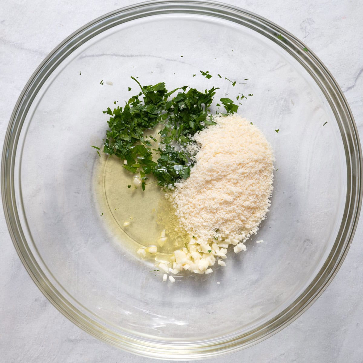 Oil, garlic, parmesan cheese and chopped parsley in a bowl before mixing.