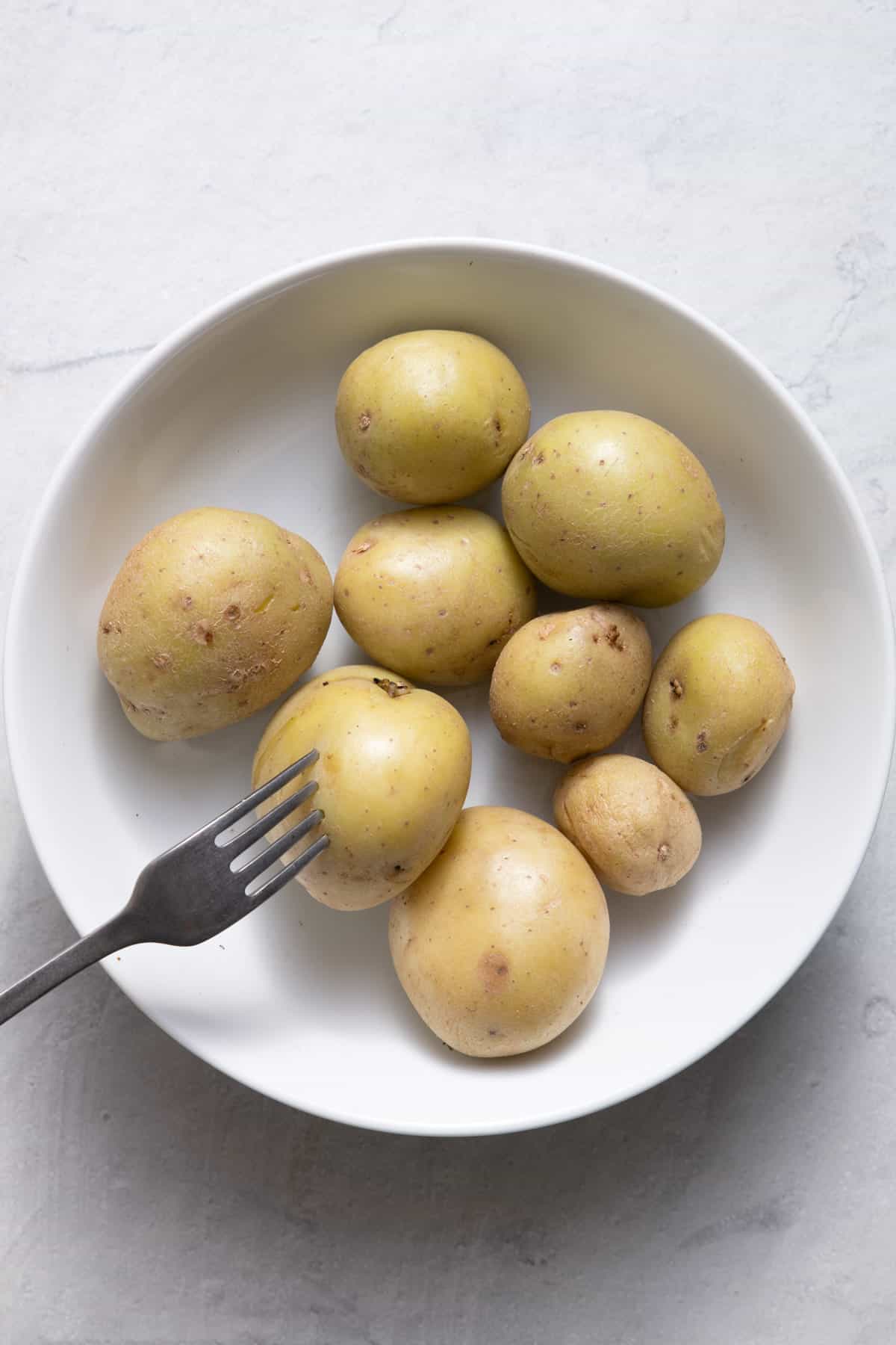 Fork piercing a baby potato to show doneness.