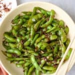 Spicy edamame on plate, a pod opened, with chopsticks resting on plate.