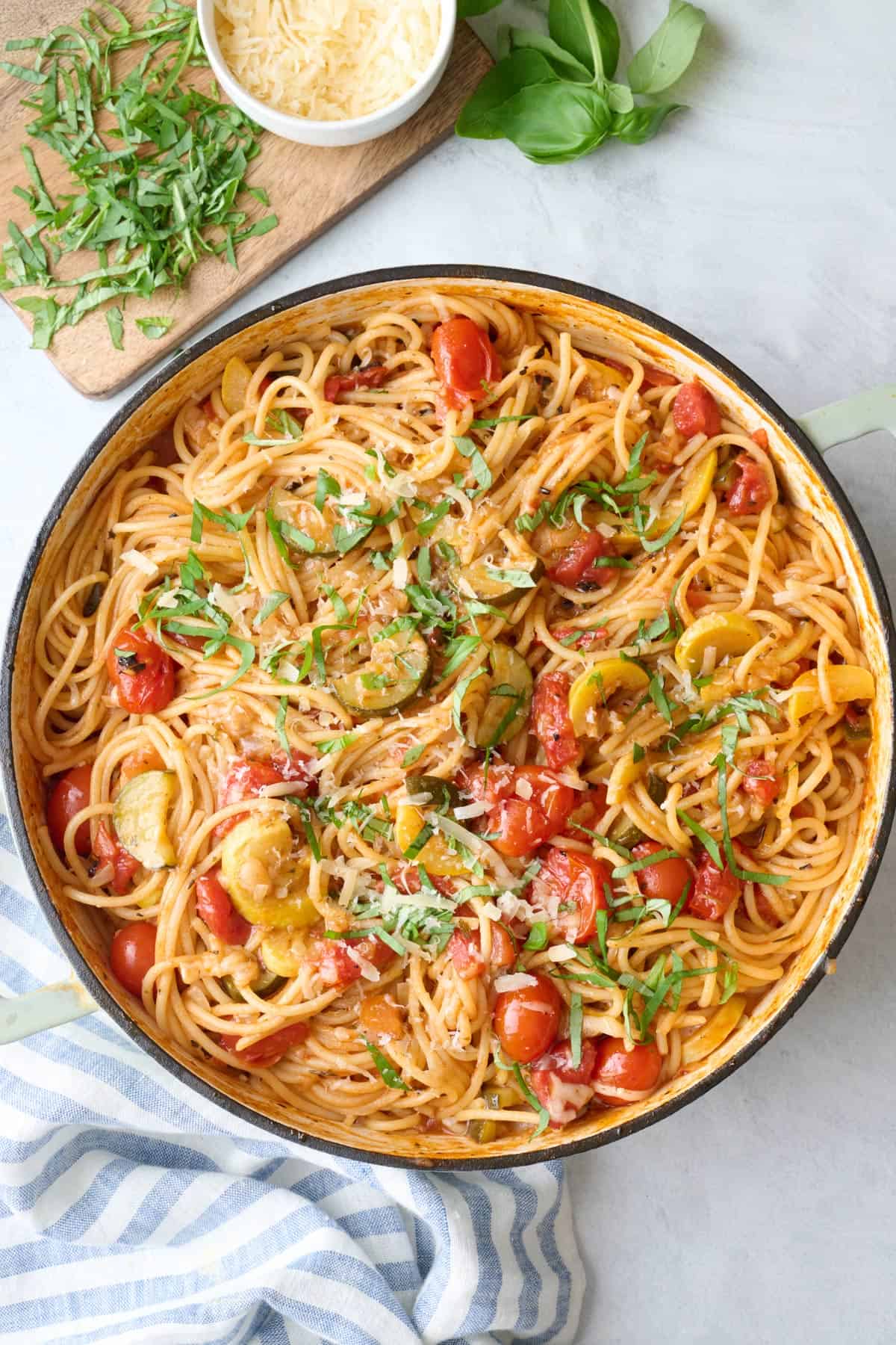 One pot veggie spaghetti garnished with parmesan and basil, small dish of extra cheese nearby.