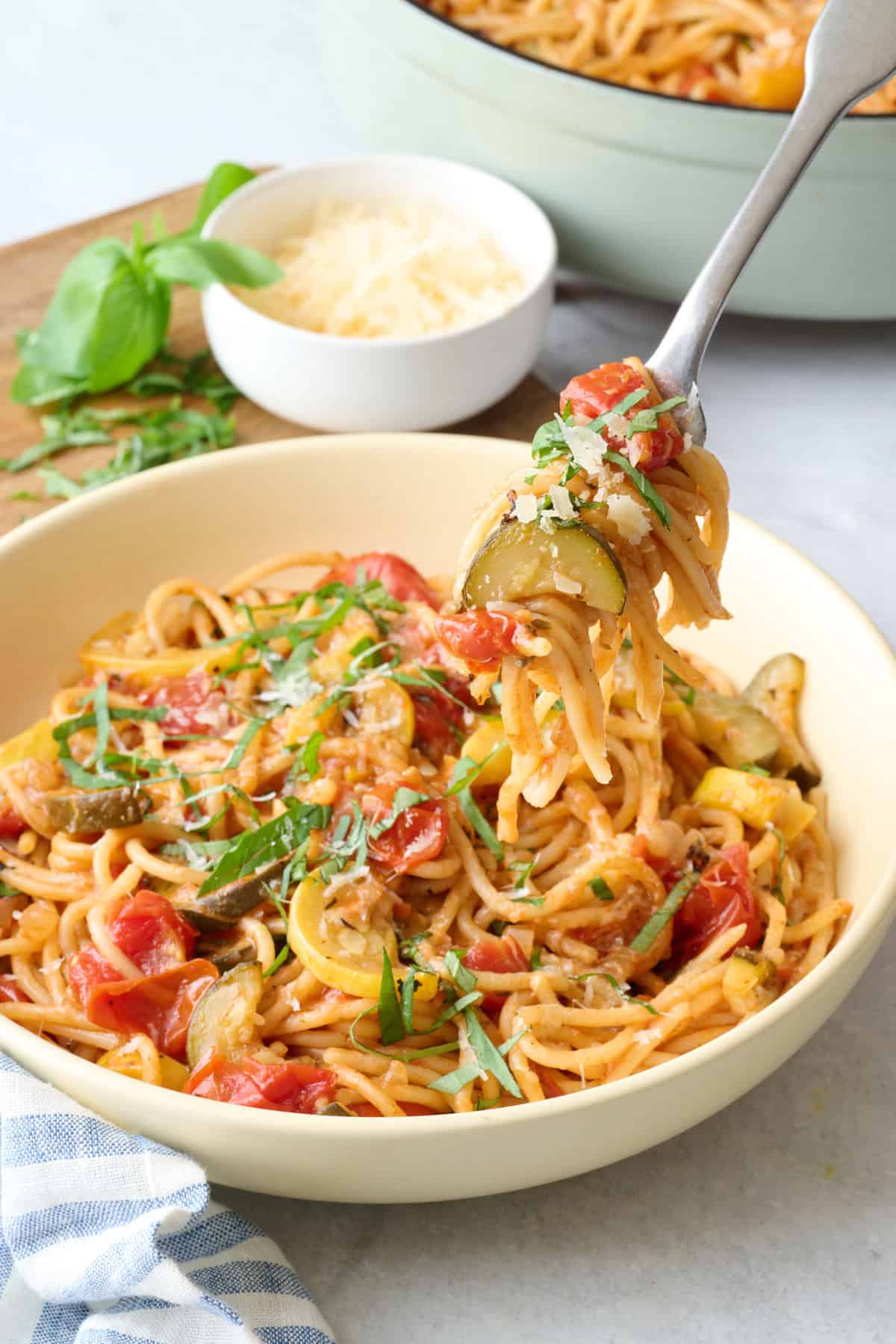Easy veggie spaghetti recipe in a shallow pasta bowl with a fork lifting up a bite with chunks of zucchini and tomatoes.