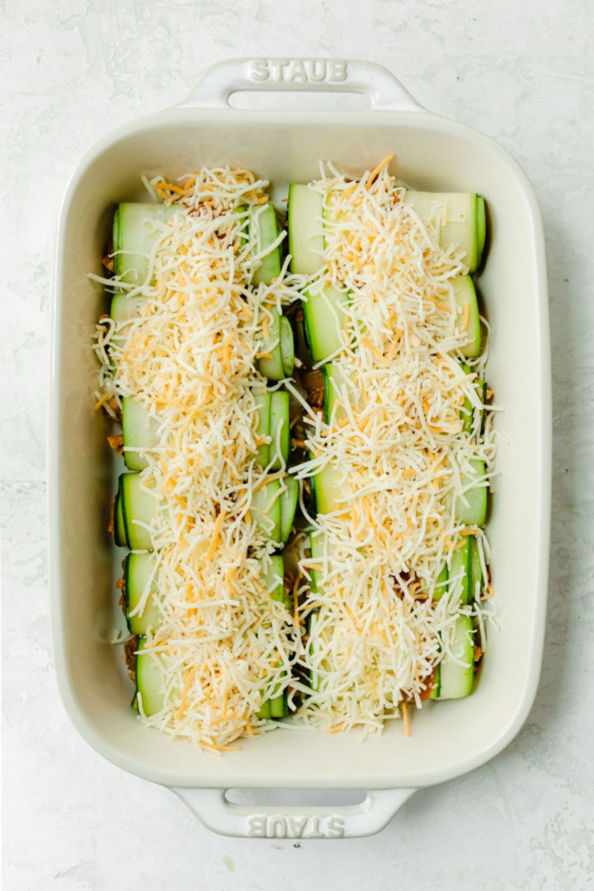 Shredded cheese added over zucchini rolls with chicken.