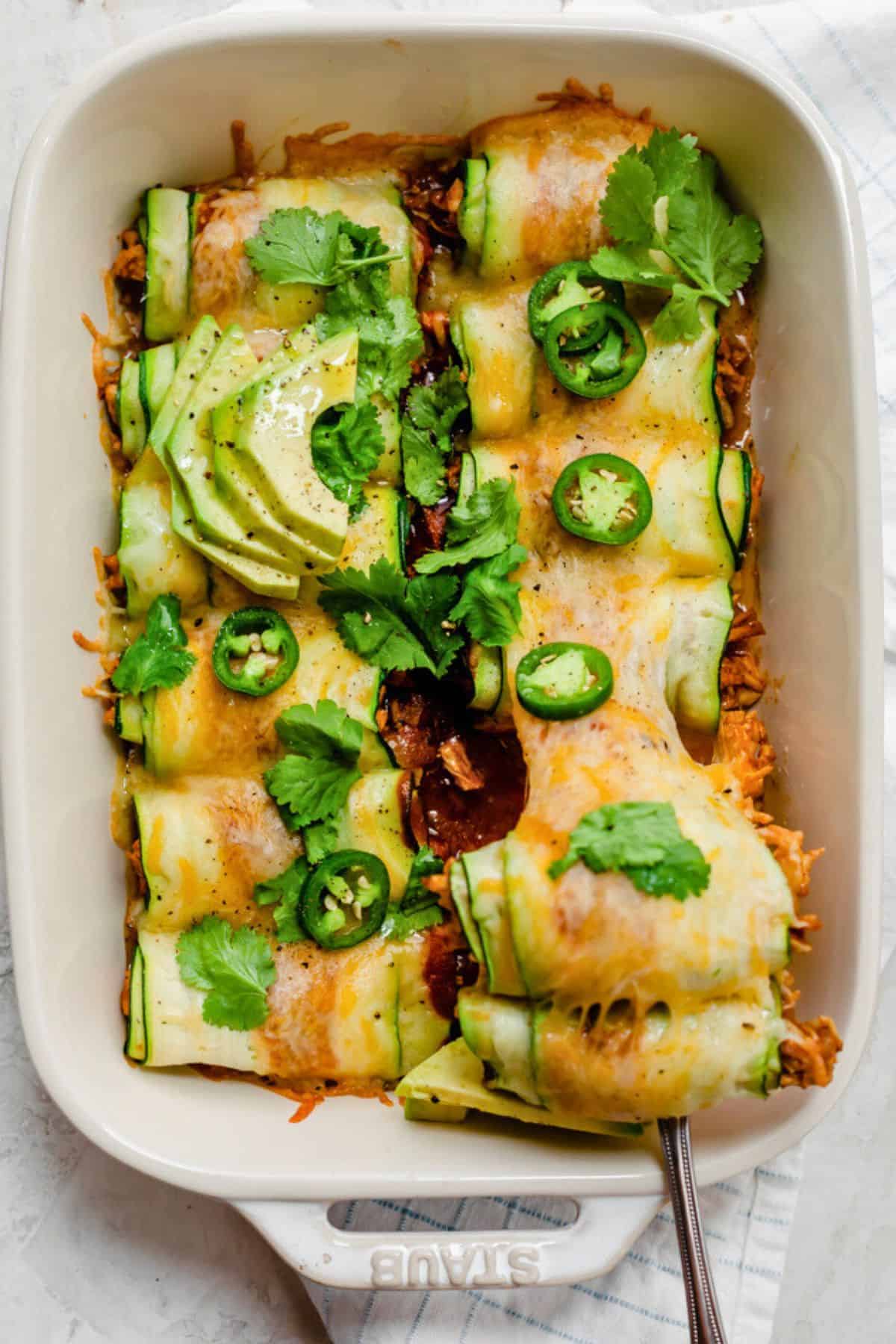 Spatula lifting up a serving of zucchini enchiladas from baking dish.