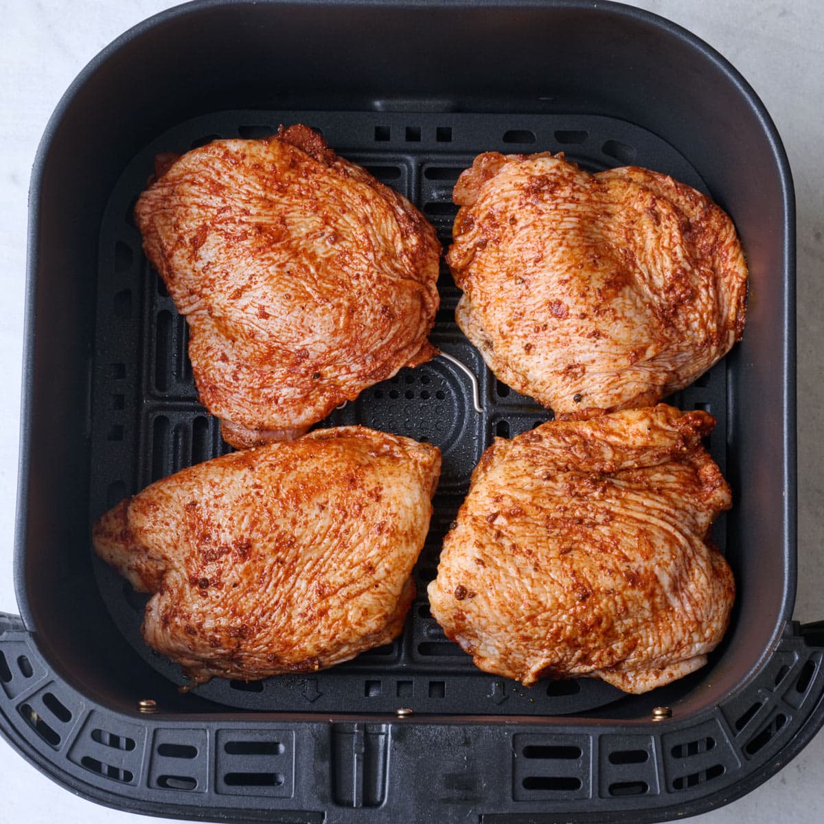 Bone in skin on chicken thighs in an air fryer basket being frying.
