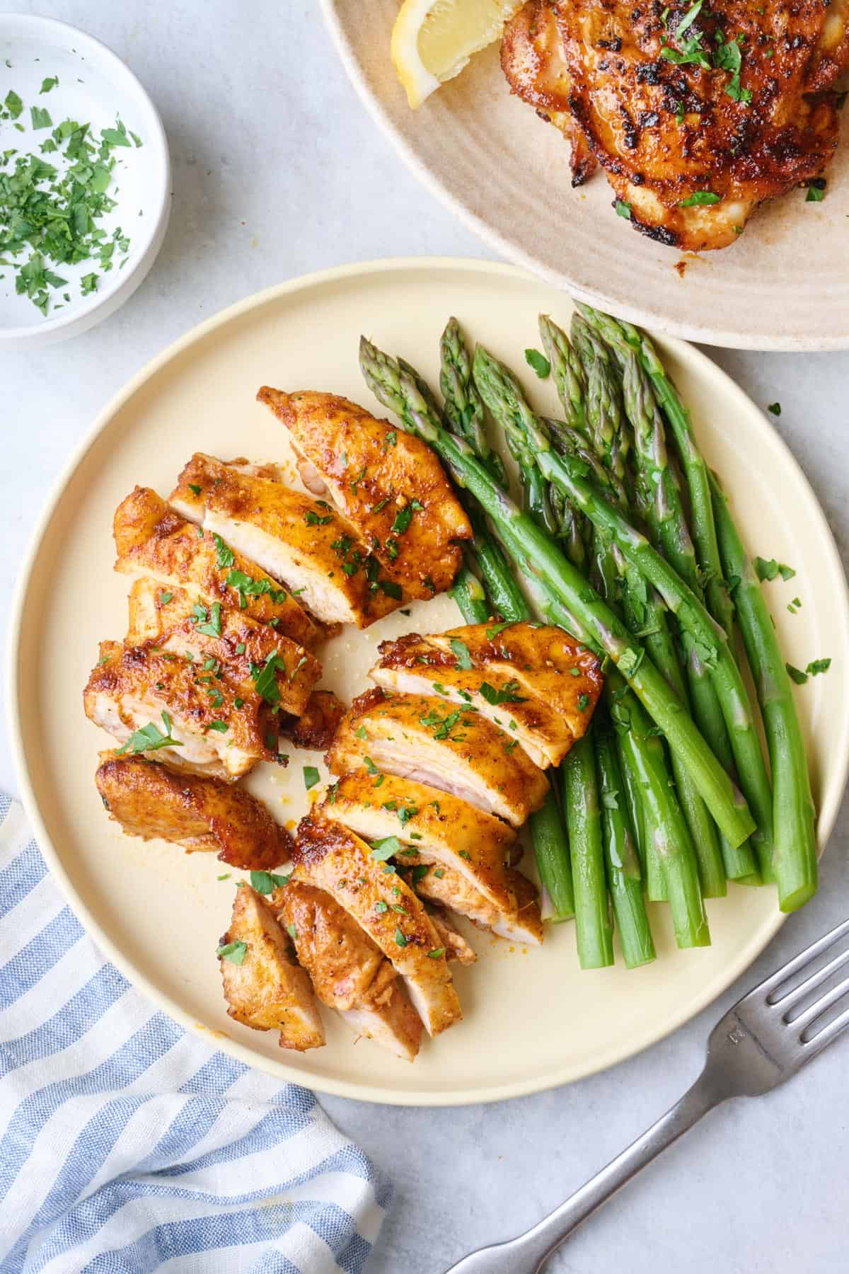 Two air fried boneless chicken thighs on a plate, sliced and served with asparagus.