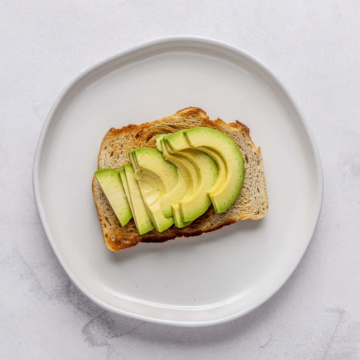 Sourdough toast with sliced avocado on a plate.