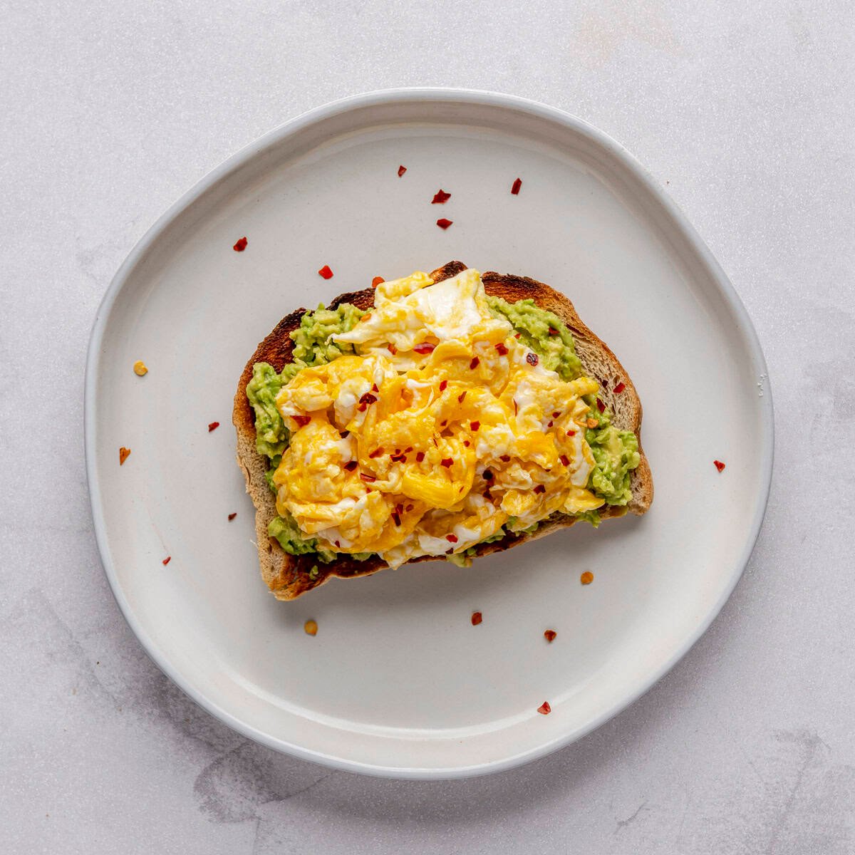 Avocado toast with scrambled eggs and red pepper flakes.