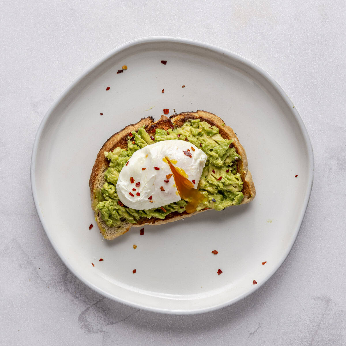 Avocado toast with poached egg, whites done with runny yolk with red pepper flakes.