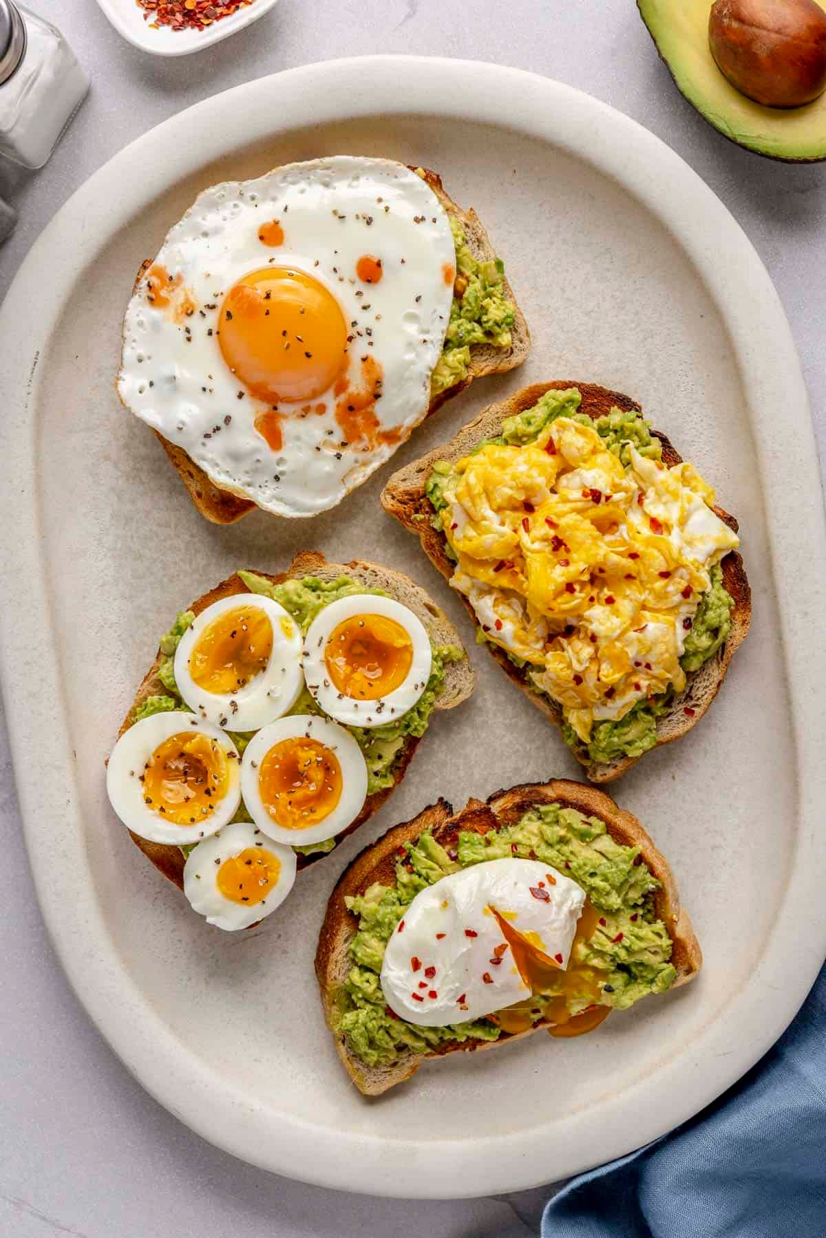 Avocado toast with 4 different styled eggs: sunny side up, scrambled, sliced boiled eggs, and poached.