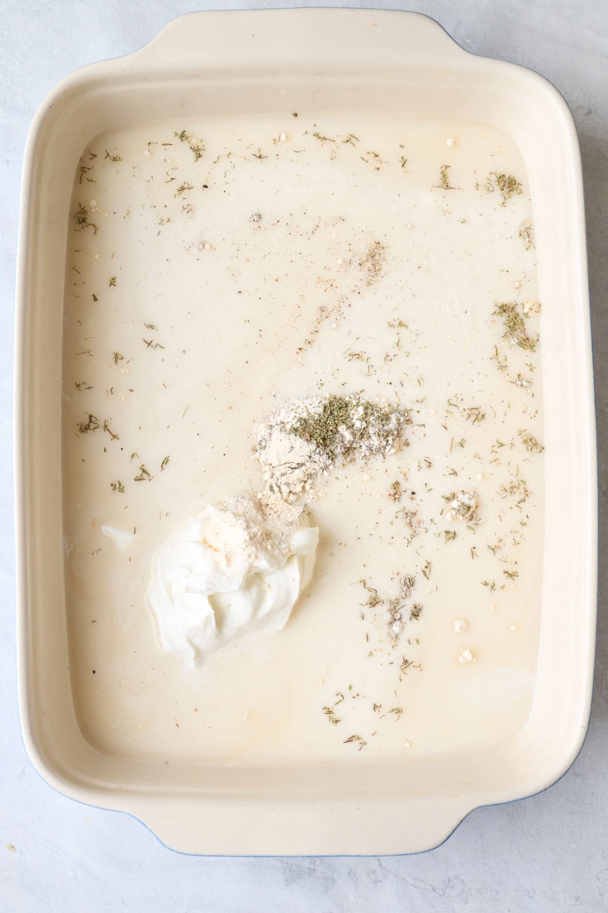 Broth, milk, yogurt, and seasonings in a casserole dish before mixing.