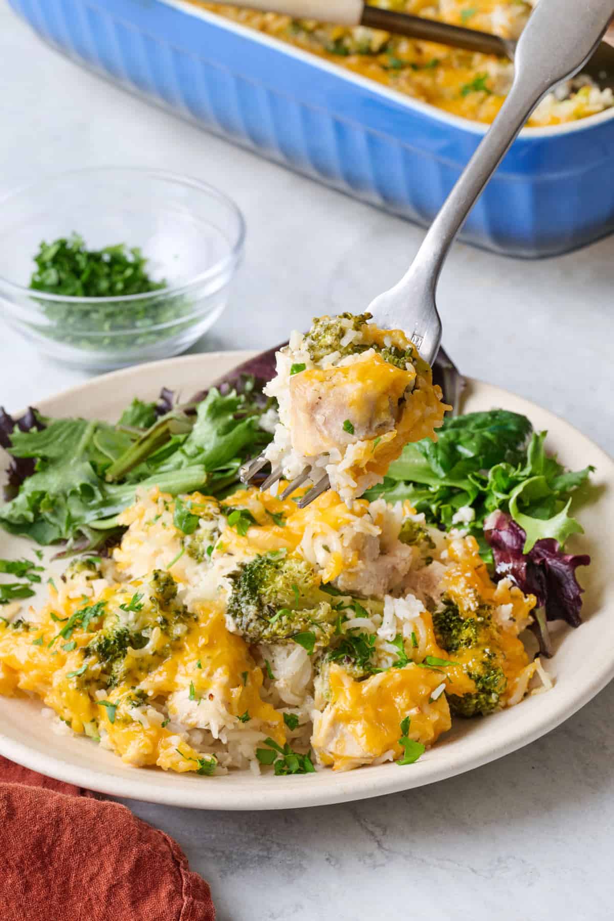 Serving of casserole on a plate with a light salad, fork lifting up a bite of chicken, broccoli and rice.