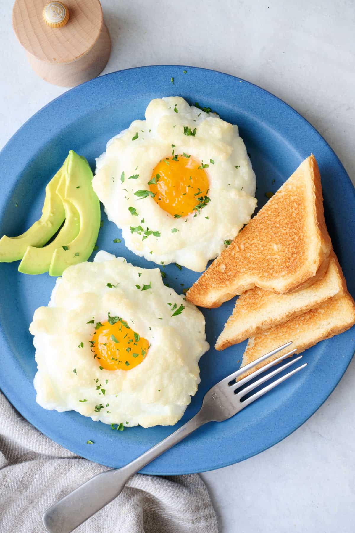 2 cloud eggs on a plate with toast triangles and avocado slices.