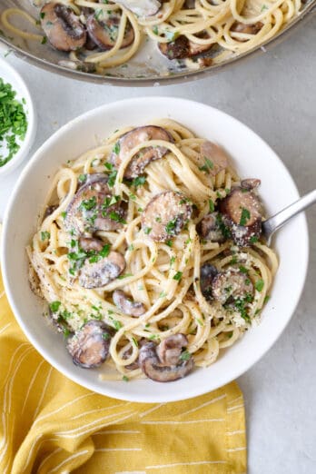 Serving of creamy parmesan mushroom pasta on a plate with pan nearby.