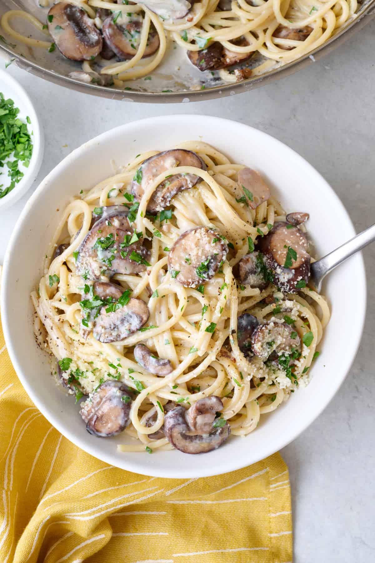 Serving of creamy parmesan mushroom pasta on a plate with pan nearby.