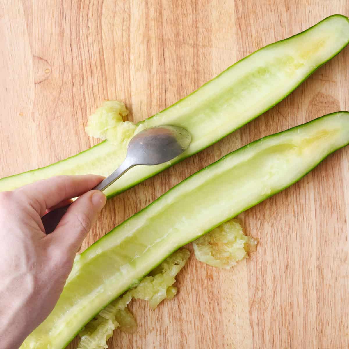 Cucumber sliced in halved lengthwise with a spoon scooping out seeds.