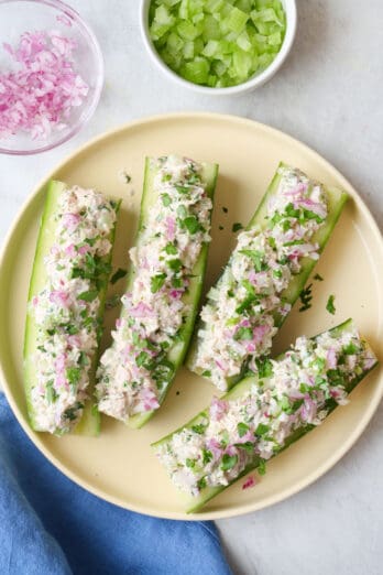 4 cucumber tuna salad boat halves on a plate garnished with fresh parsley, extra fresh ingredients nearby.