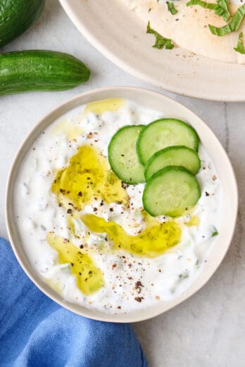 Easy cucumber yogurt sauce in a bowl with sliced cucumbers and a drizzle of olive oil on top.