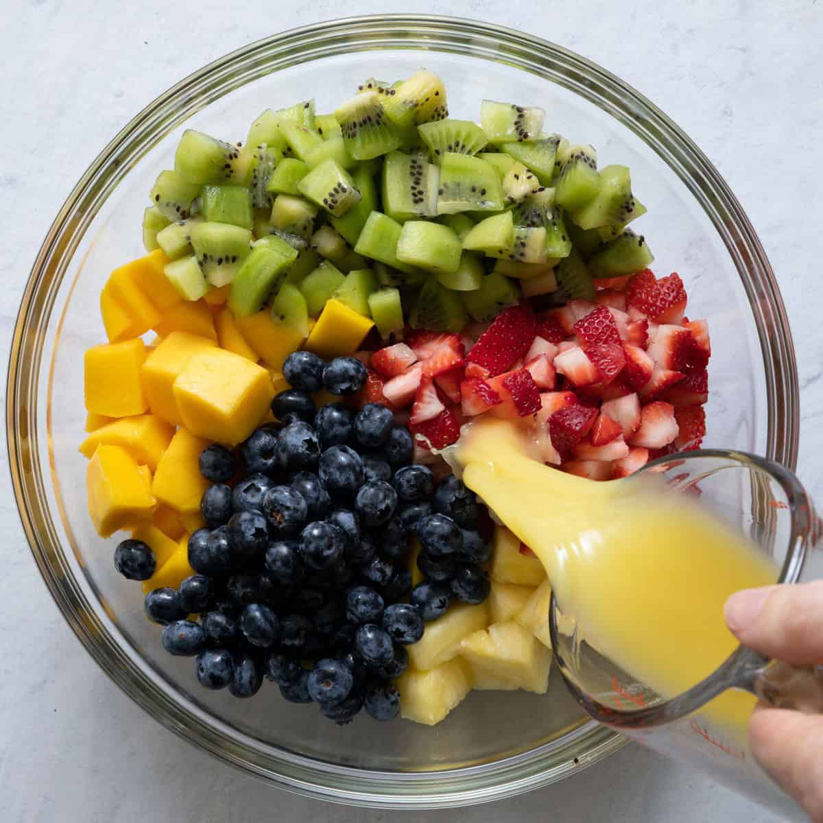 Adding orange juice to mixed fruit bowl.