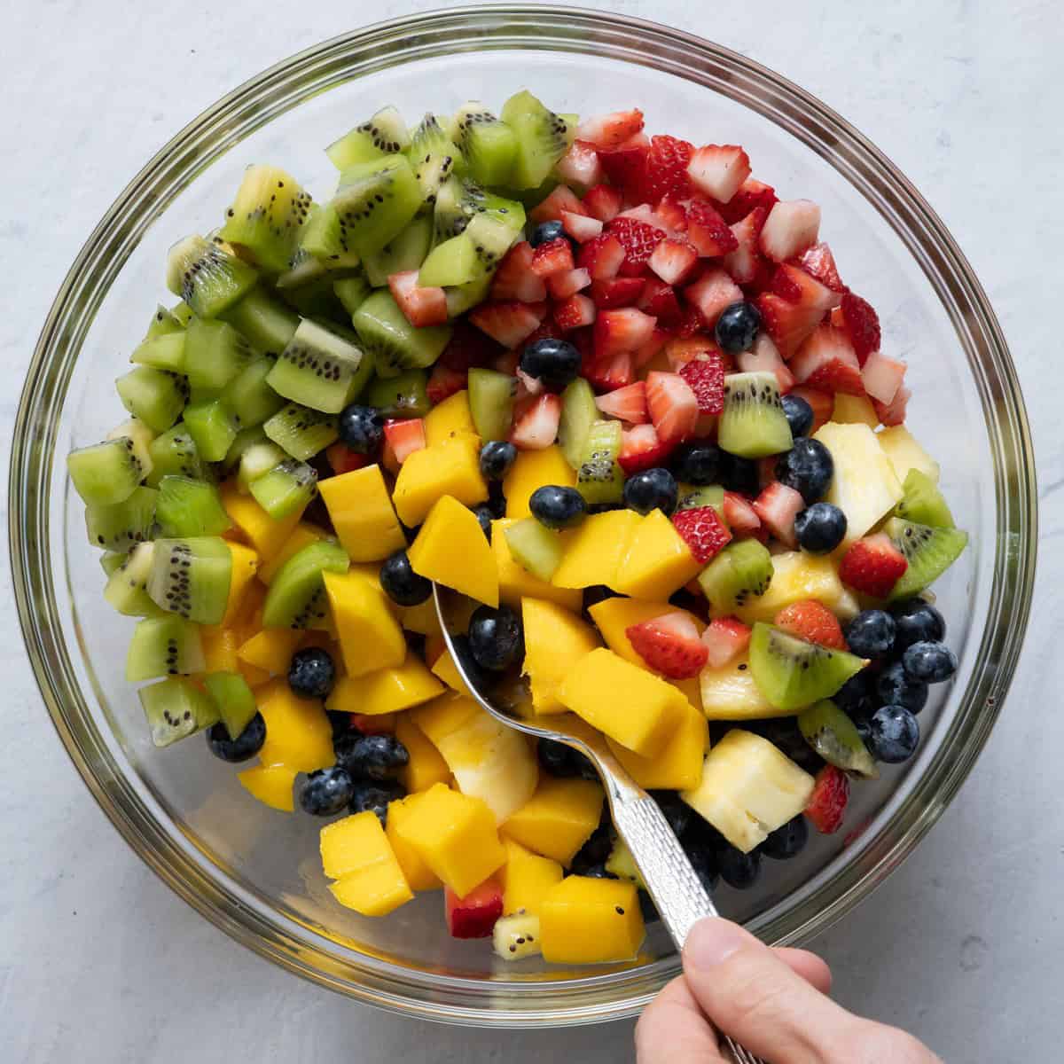 Tossing fruit salad with sauce.