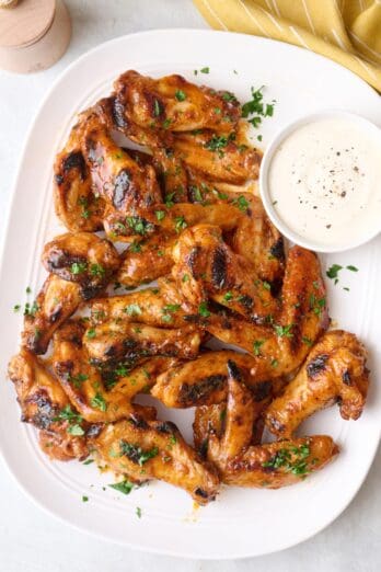 Grilled chicken wings on a platter with a side of ranch in a small bowl.
