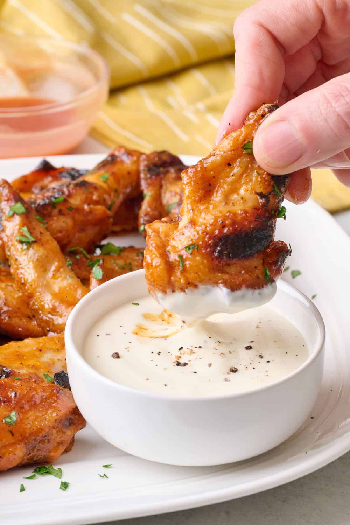 Dipping a sauced grilled chicken wing into ranch on a plate of more wings.