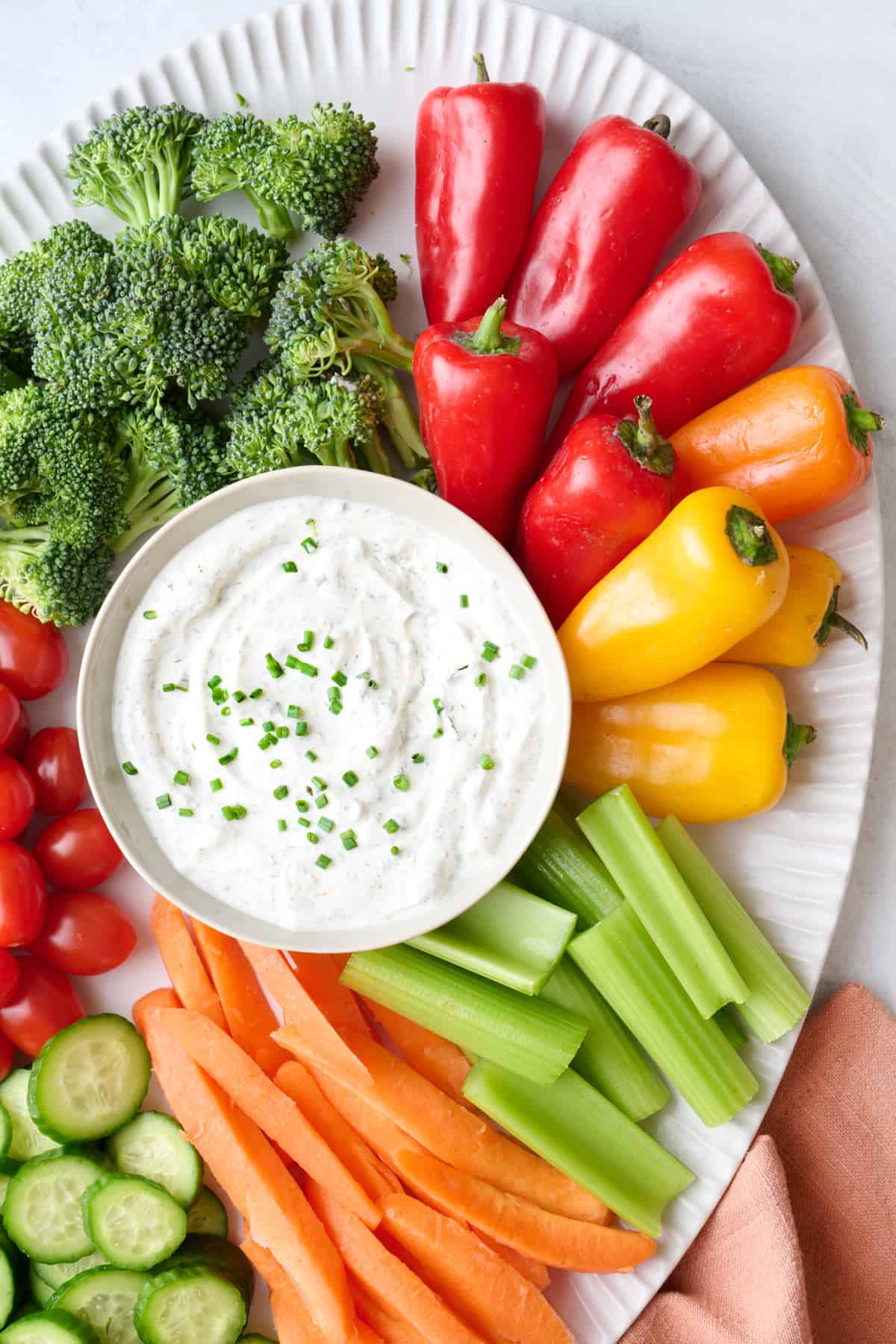 Easy ranch dip recipe in a bowl on a platter with broccoli florets, mini peppers, cherry tomatoes, celery and carrot sticks, and sliced cucumbers.