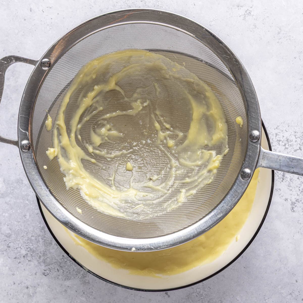 Pudding poured over a fine mesh sieve into a bowl below to show any bits in the strainer.