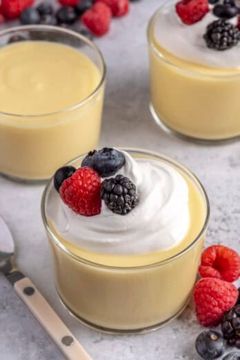 Homemade vanilla pudding in small dessert glasses, topped with whipped cream and fresh berries.