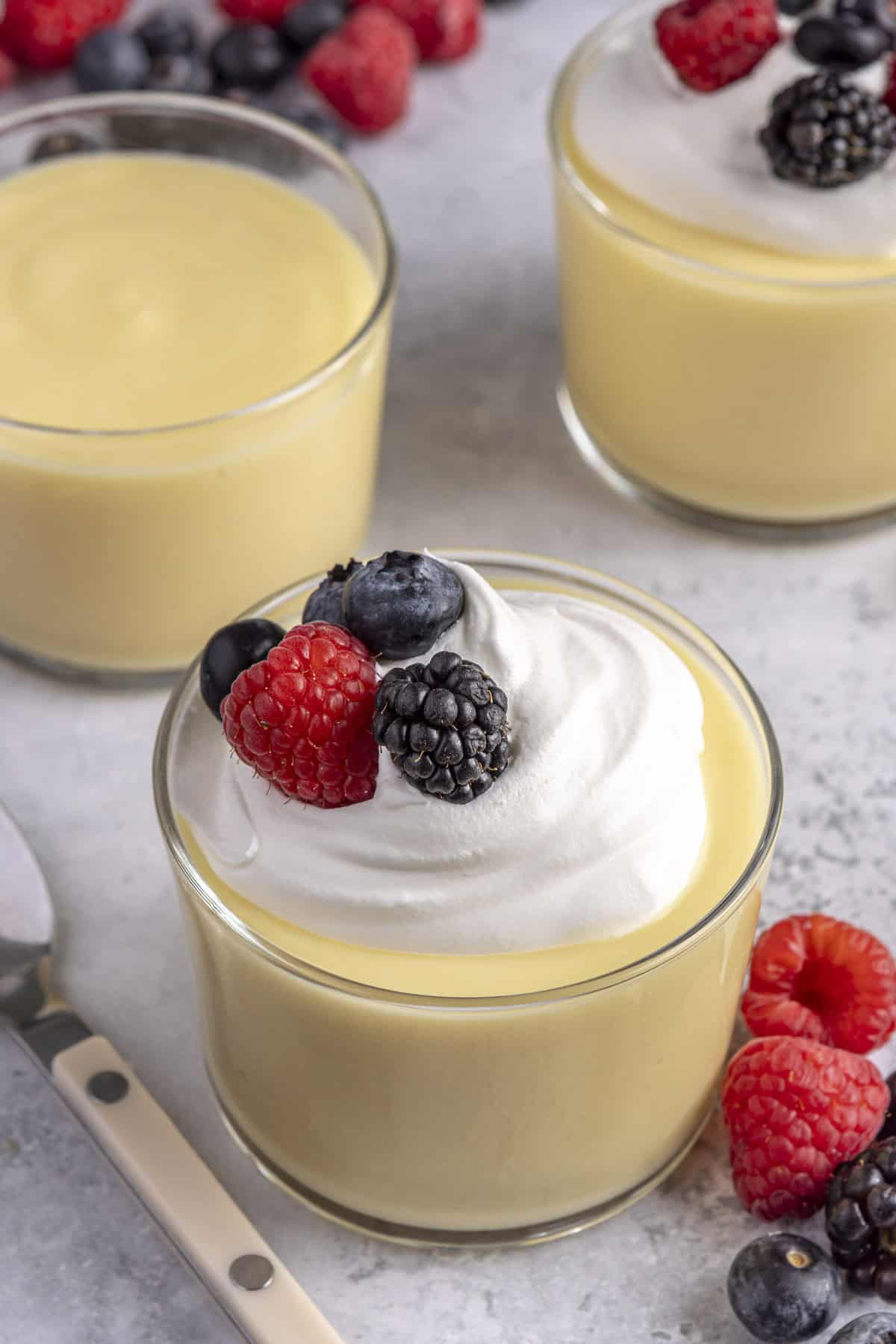 Homemade vanilla pudding in small dessert glasses, topped with whipped cream and fresh berries.