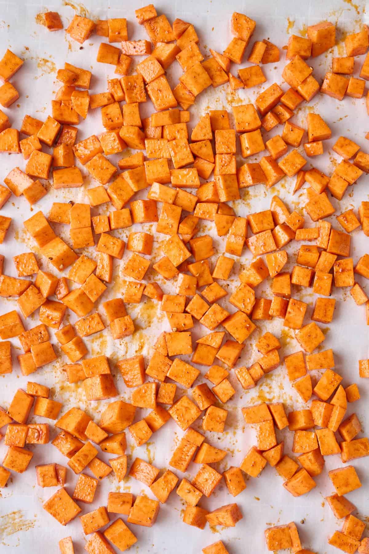 Diced sweet potatoes tossed with oil and seasonings before roasting.