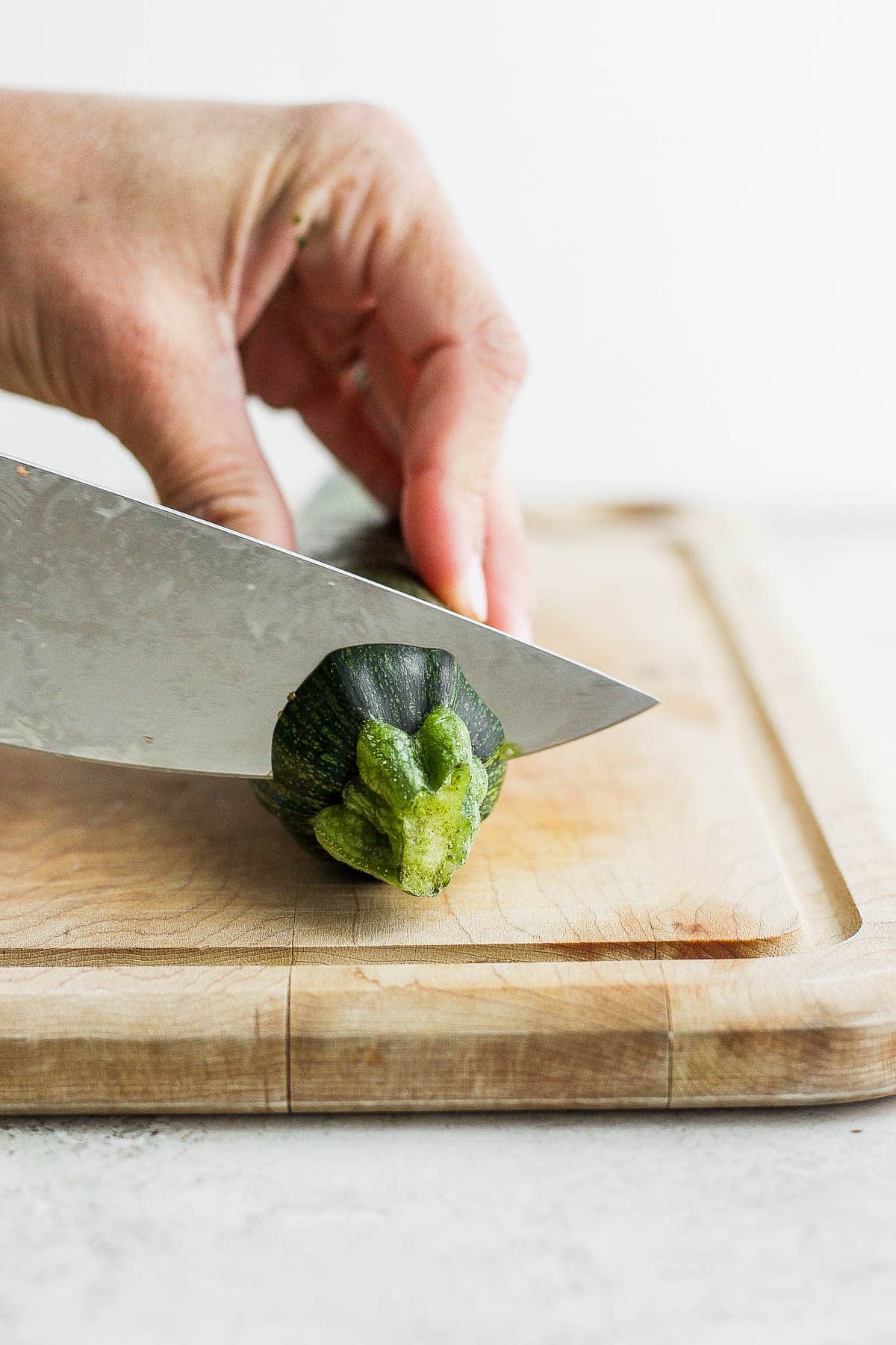 Zucchini on a cutting board with top being cut off.