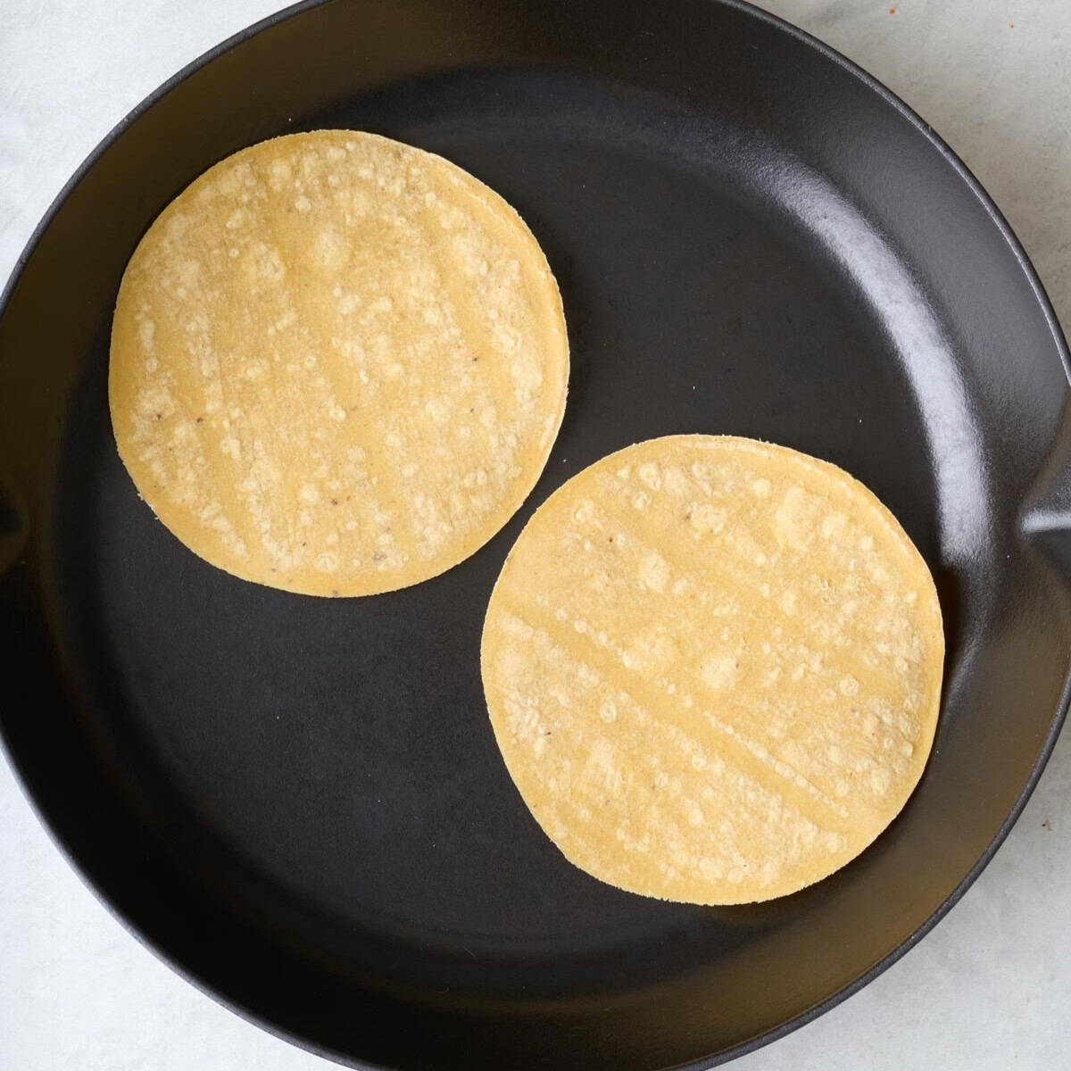 Corn tortillas in a skillet.
