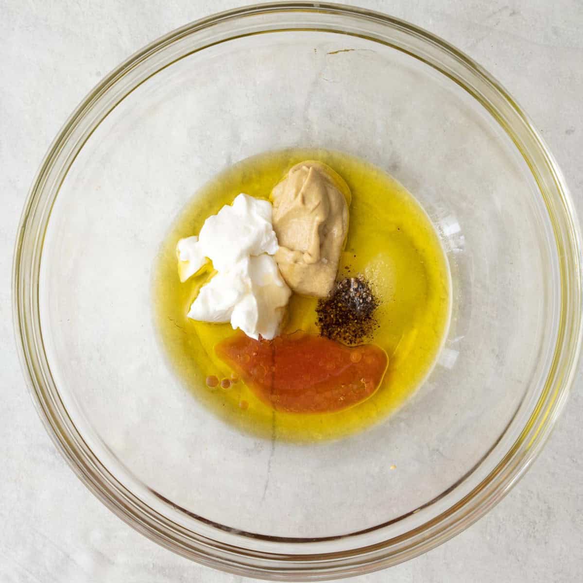 Dijon mustard, yogurt, vinegar, honey, pepper and oil in a bowl before whisking.