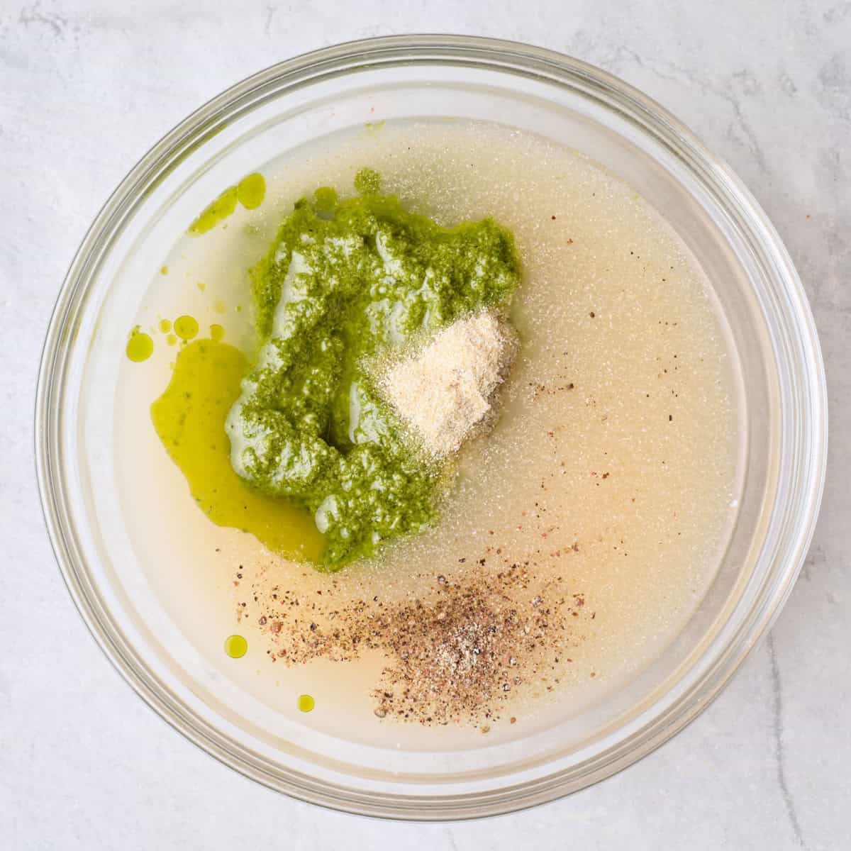 Broth, pesto, yogurt, onion powder, salt and pepper in a bowl before mixing.