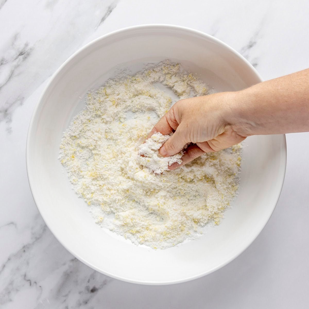 Hand rubbing sugar and lemon zest in a bowl.