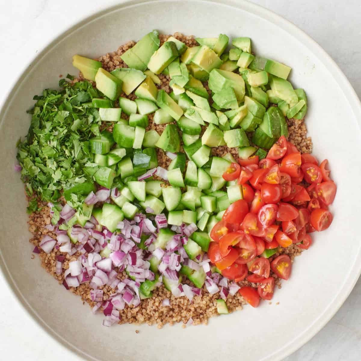 Chopped avocado, tomatoes, red onions, and cilantro over cooked quinoa in a bowl.