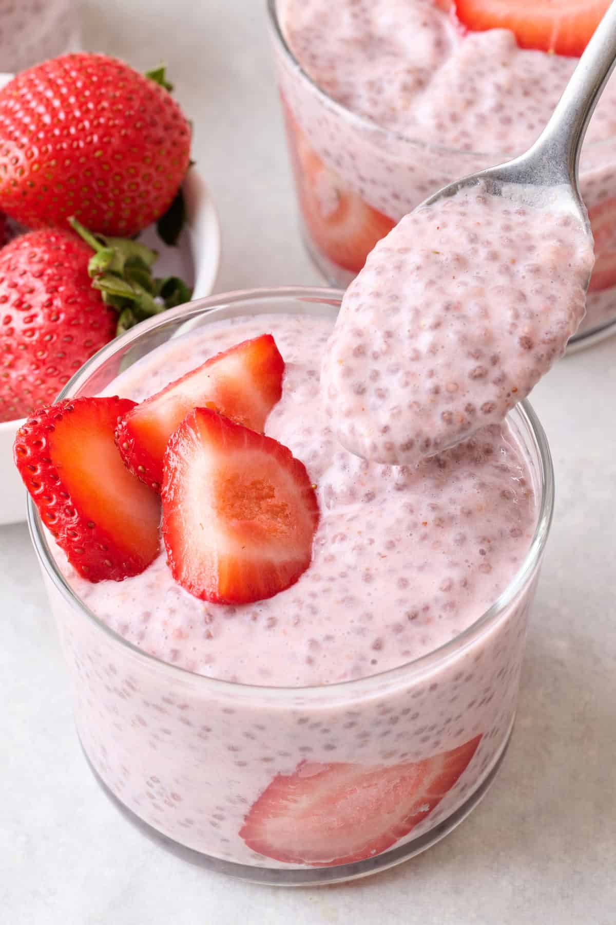 Spoon lifting up a bite of strawberry chia pudding topped with fresh berries.