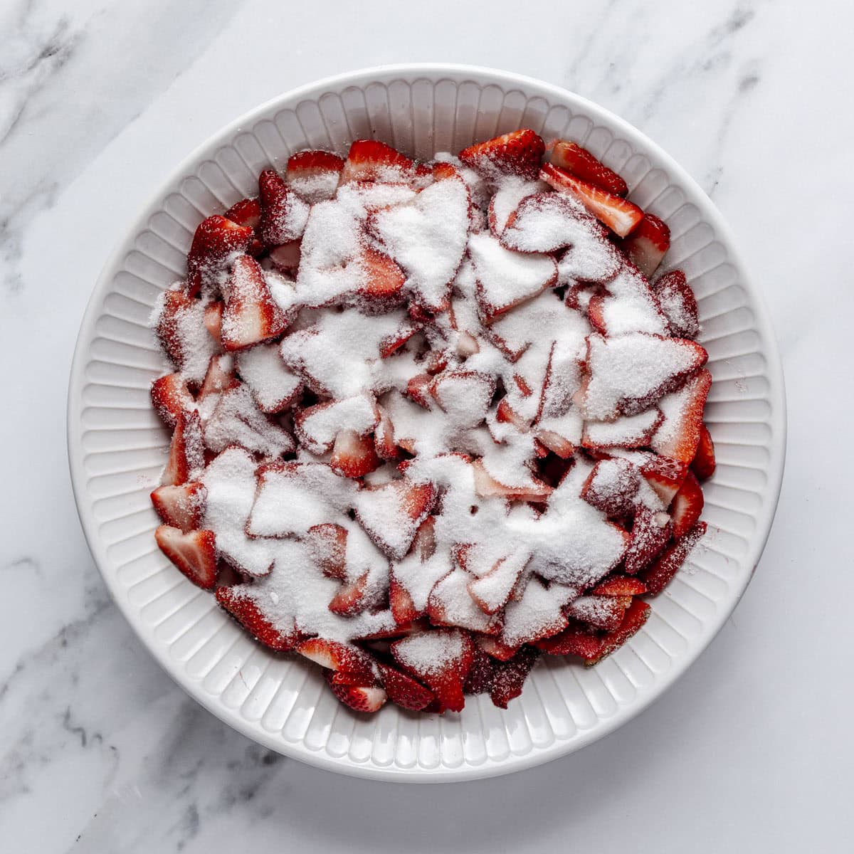 Sliced strawberries and sugar in a bowl before mixing.