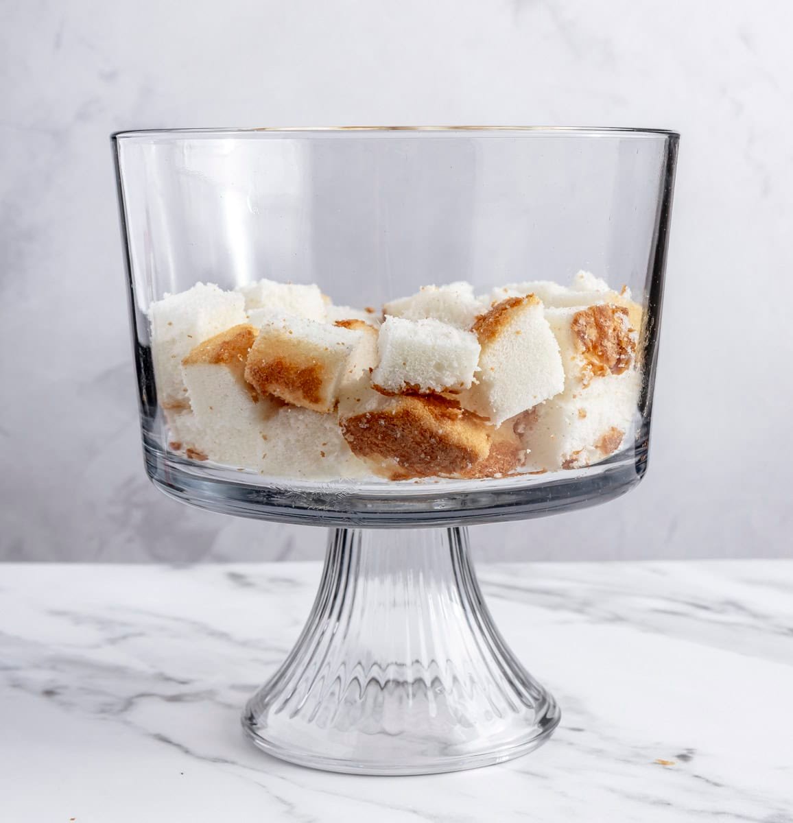 Half of the angel food cake cubes layered in the bottom of a trifle dish.