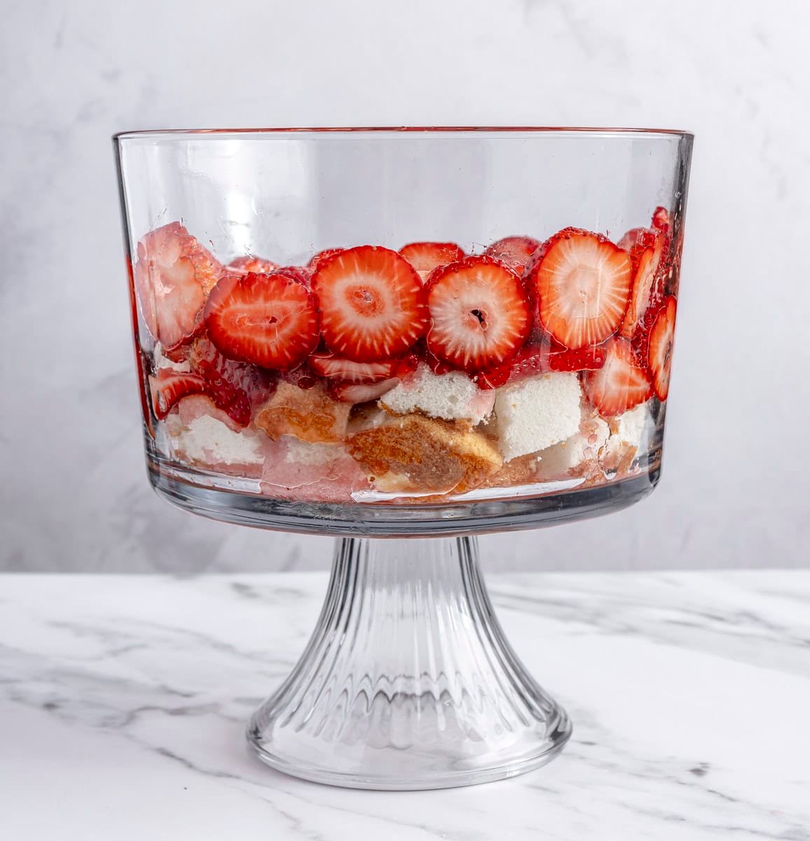 Sliced macerated strawberries and juices added on top of cake pieces.