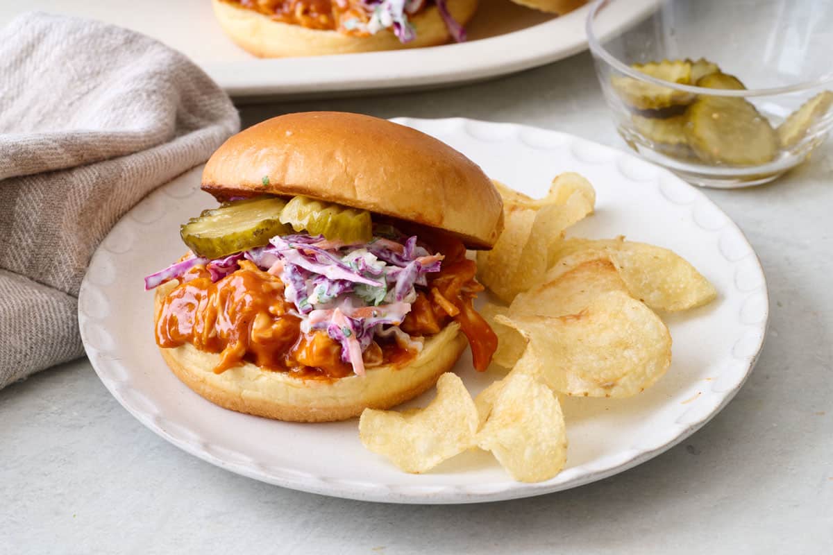 Homemade bbq shredded chicken sandwich with coleslaw on a plate with chips.