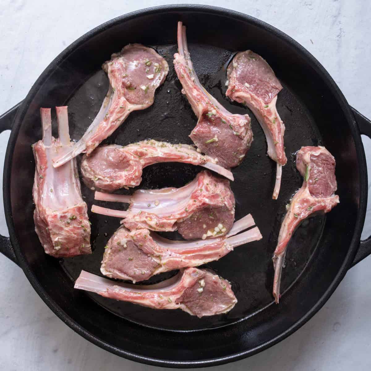 Seasoned lamb chops in an oiled cast iron skillet before baking.