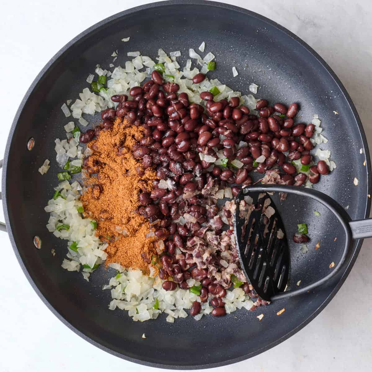 Black beans, taco seasoning and salt added with potato masher just starting to mash some beans.