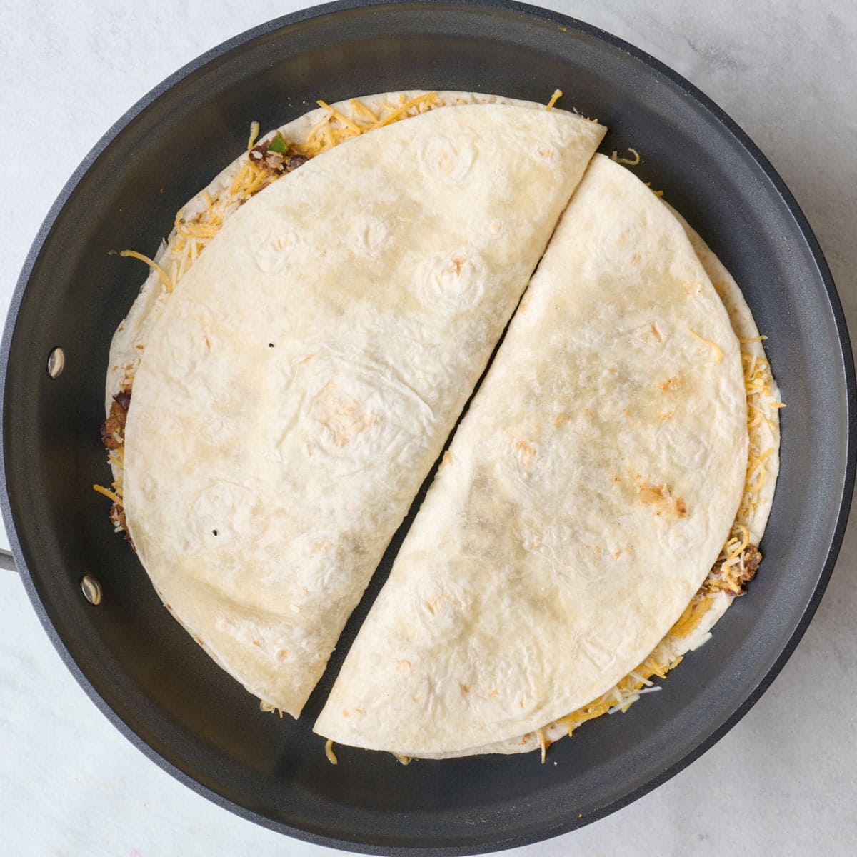 Two folded quesadillas on skillet.