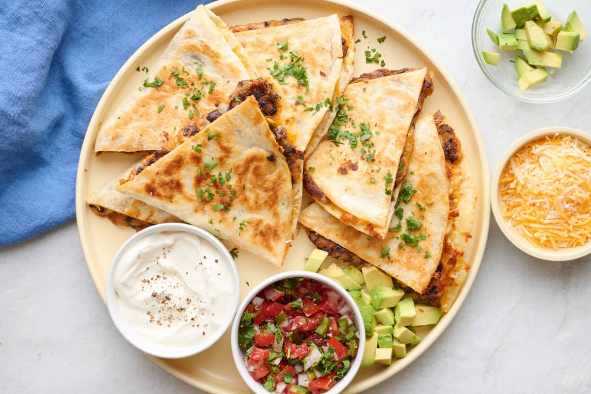 Easy black bean quesadilla on a platter with a side of sour cream, salsa, and avocado.