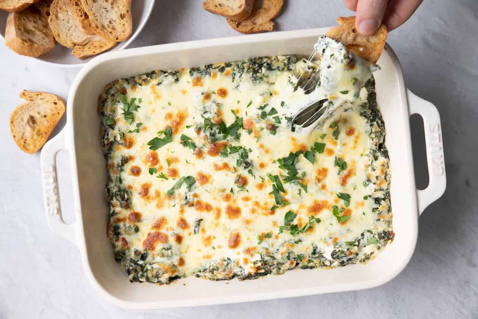 Toasted bread being dipped in Skinny Spinach Dip