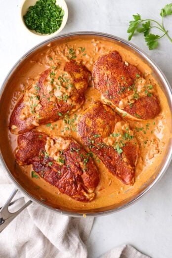 Creamy cajun chicken in the skillet with cream sauce, lightly drizzled over chicken.